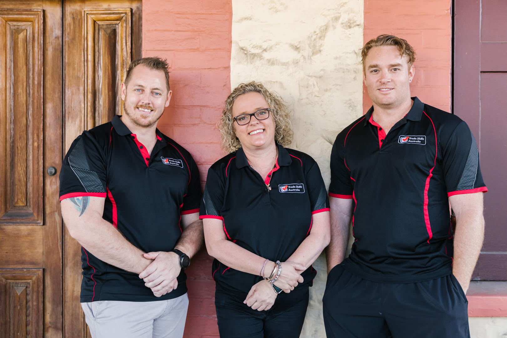 Three of the Trade Skills Australia team in black and red shirts posing and smiling