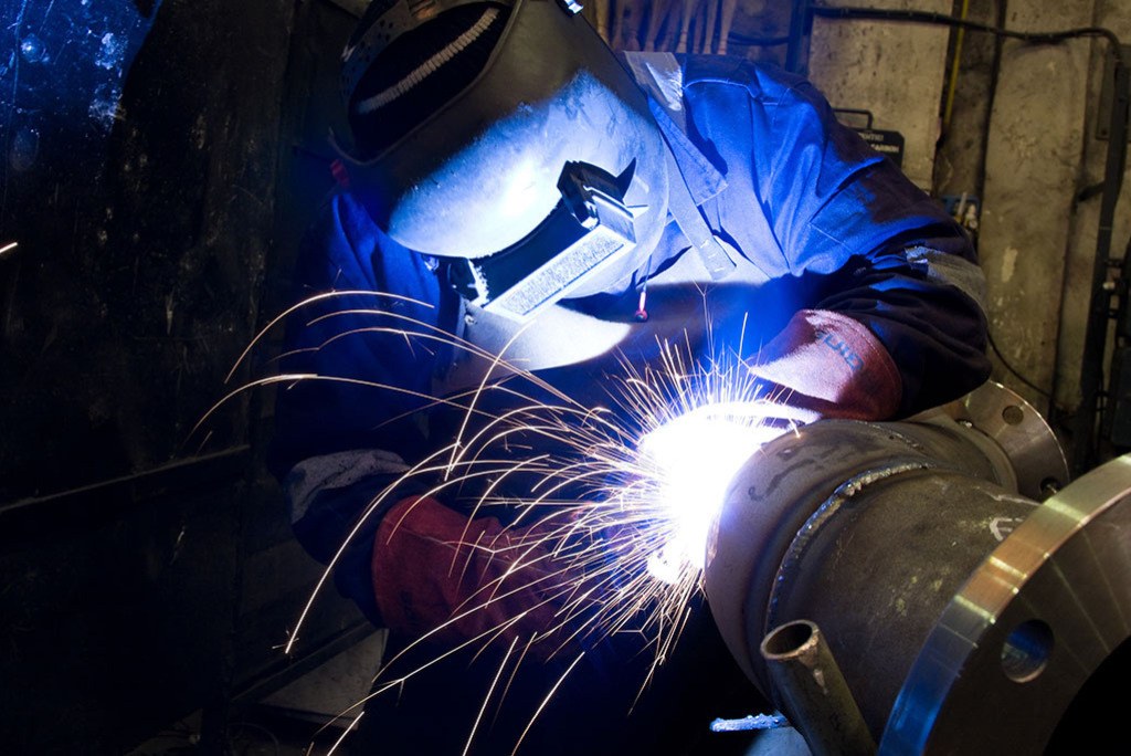Metalworker welding a metal pipe with a welding torch, producing bright sparks