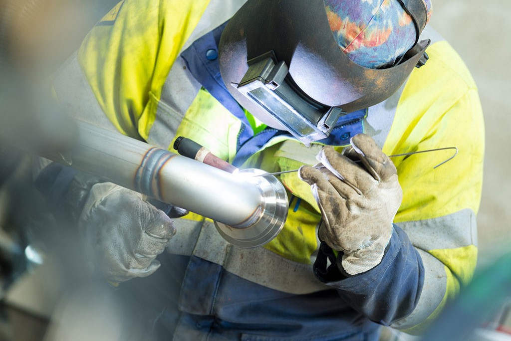 Engineer in safety equipment, wearing a welding helmet and gloves, preparing for metalwork, highlighting skills in welding